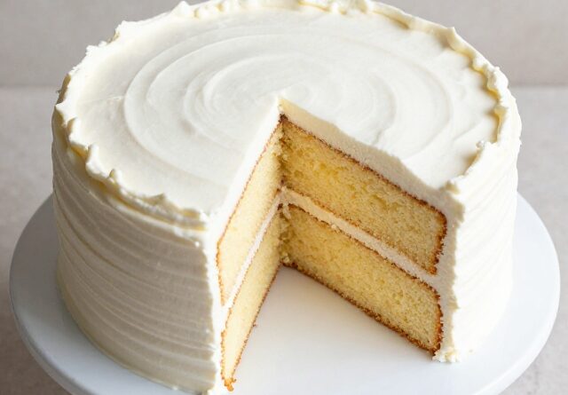 Frosted two-layer vanilla cake with a slice cut out showing soft crumb