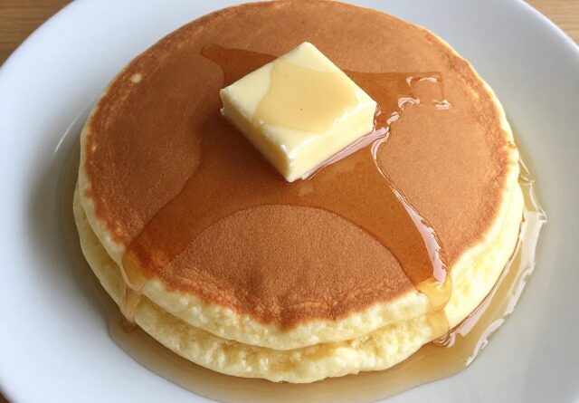 Single cottage cheese pancake with butter and syrup on a white plate