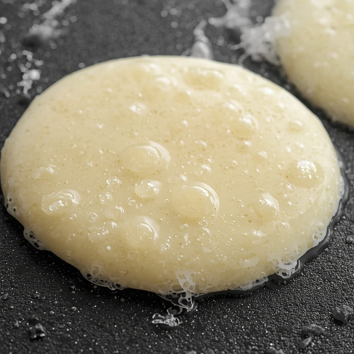 Cottage cheese pancake batter cooking on a griddle with bubbles forming