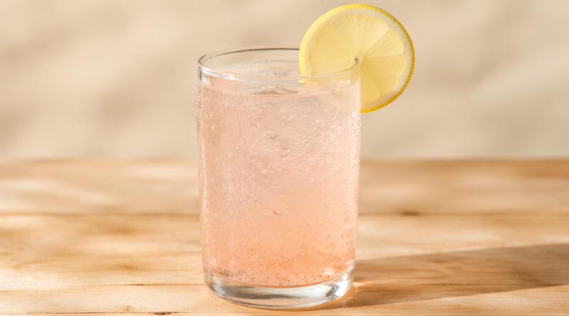 Glass of pink salt trick weight loss drink with lemon slice on wooden table