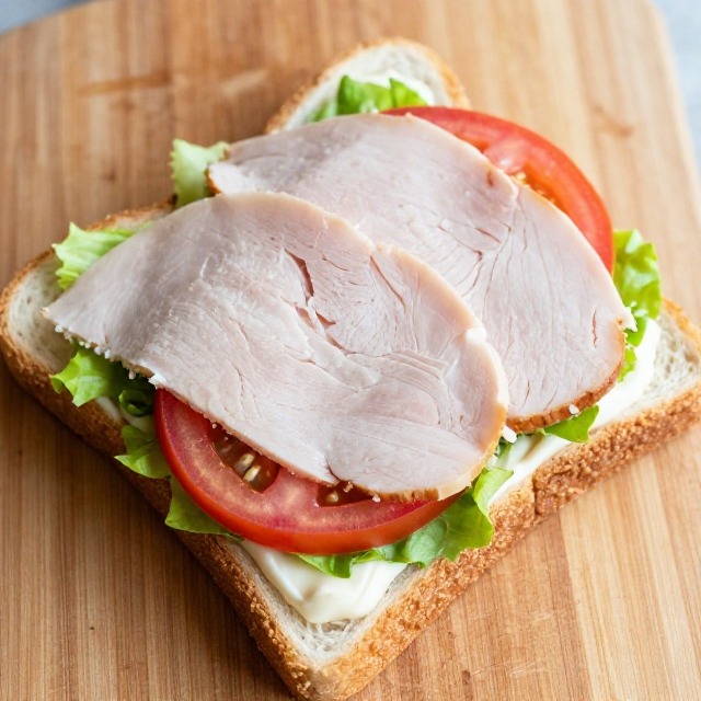 Overhead shot of the first club sandwich layer with lettuce, tomato, and turkey before the center bread slice is added