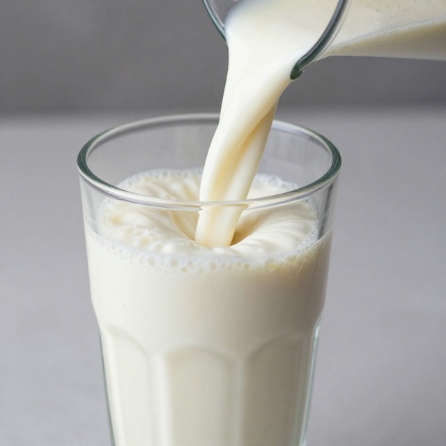 Thick protein milkshake being poured into a tall glass
