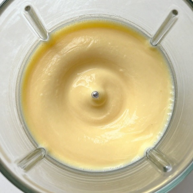 Close-up of blended cottage cheese batter in a glass blender jar, smooth and pale, no text, no labels, no background drinks or glasses of liquid
