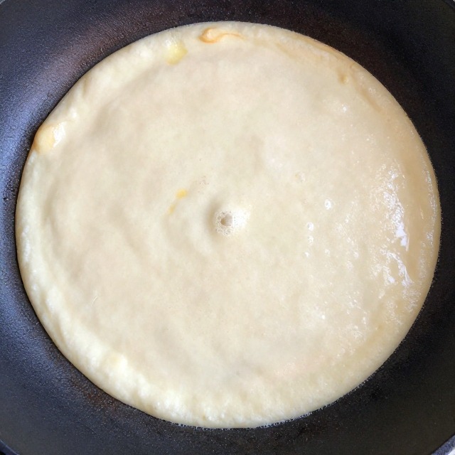 Cottage cheese pancake batter cooking on a nonstick griddle with bubbles forming on the surface, no text, no labels, no background drinks or glasses of liquid
