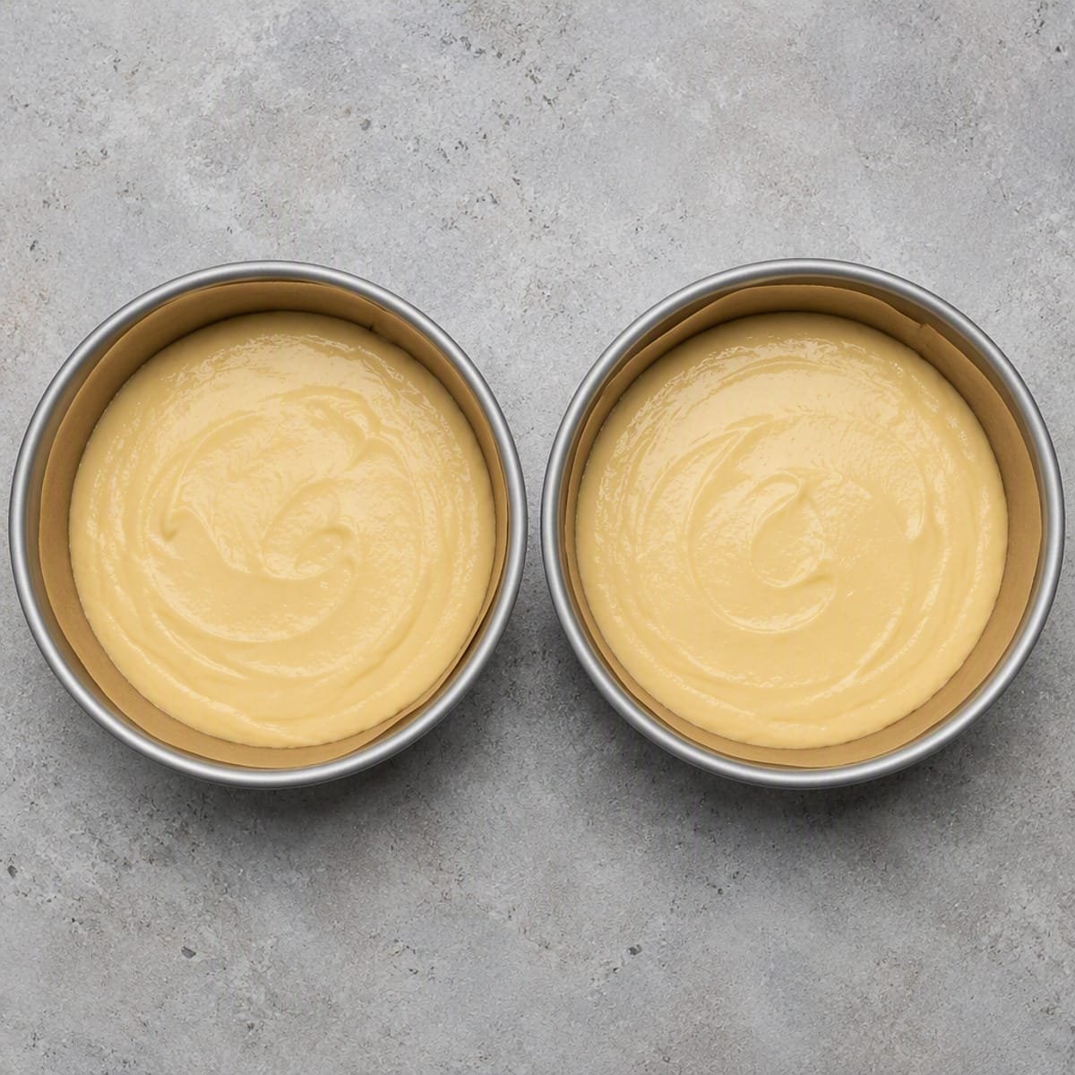 Vanilla cake batter divided evenly into round cake pans before baking