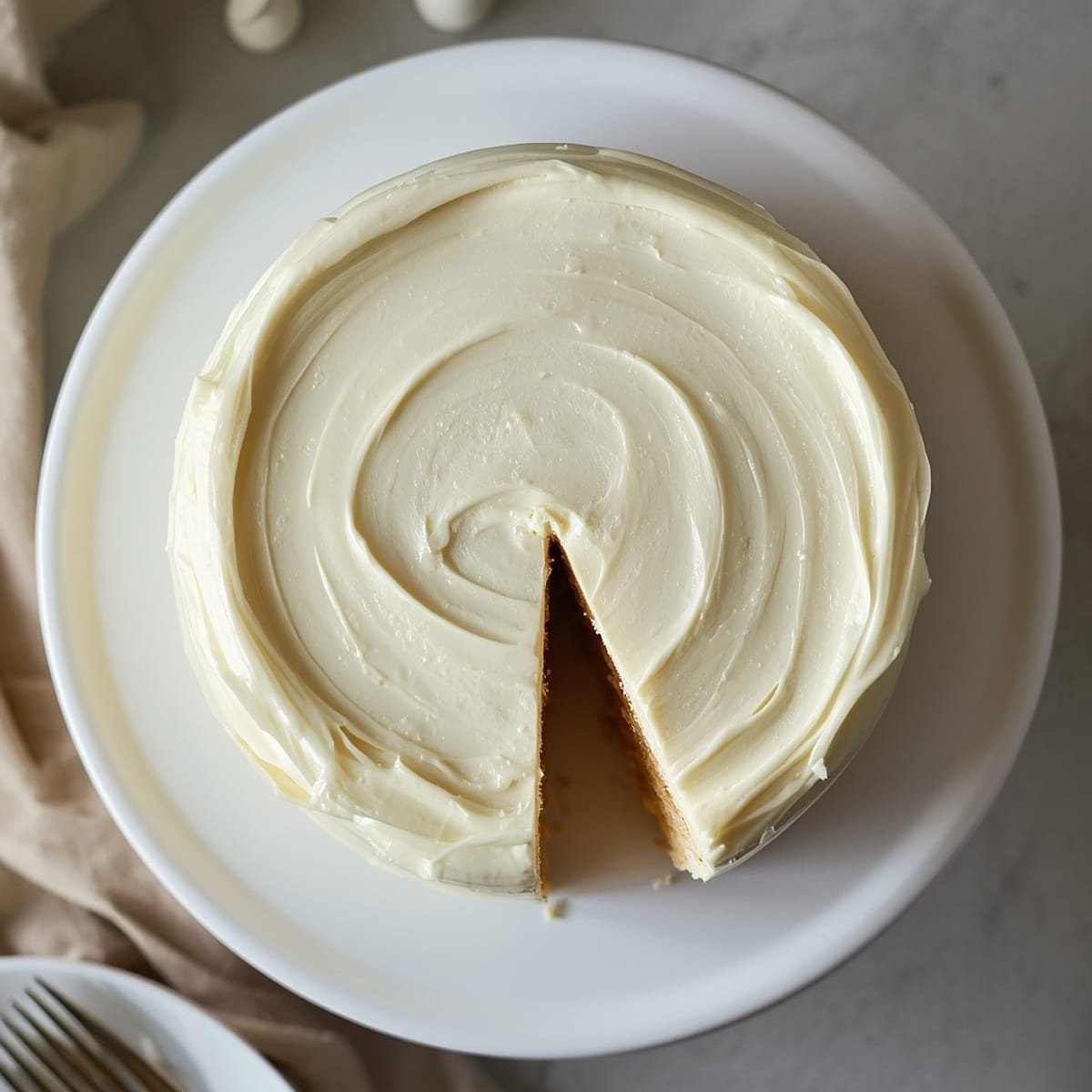 Overhead square shot of a frosted two-layer vanilla cake recipe with a slice cut out showing the soft crumb, on a white cake stand