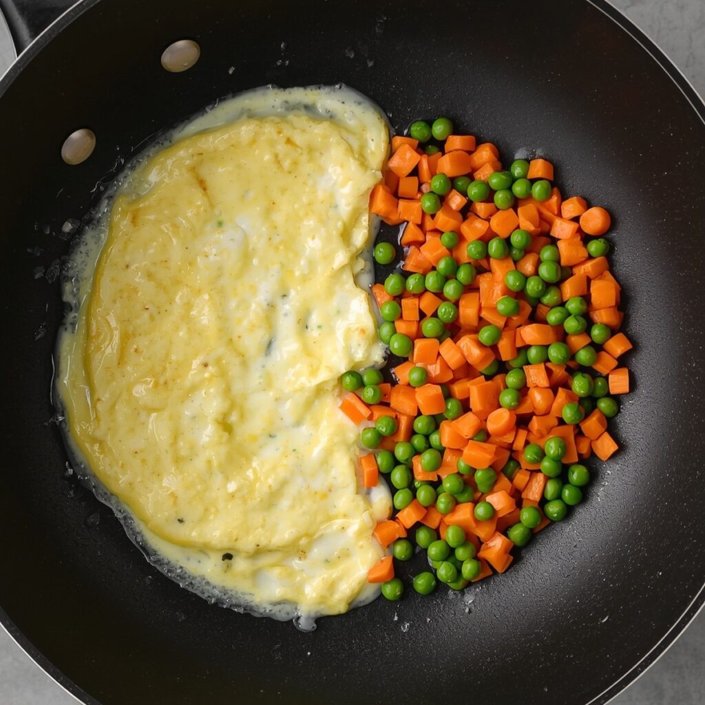 Scrambled eggs cooking on one side of a wok while vegetables cook on the other side, no text, no labels, no background drinks or glasses of liquid