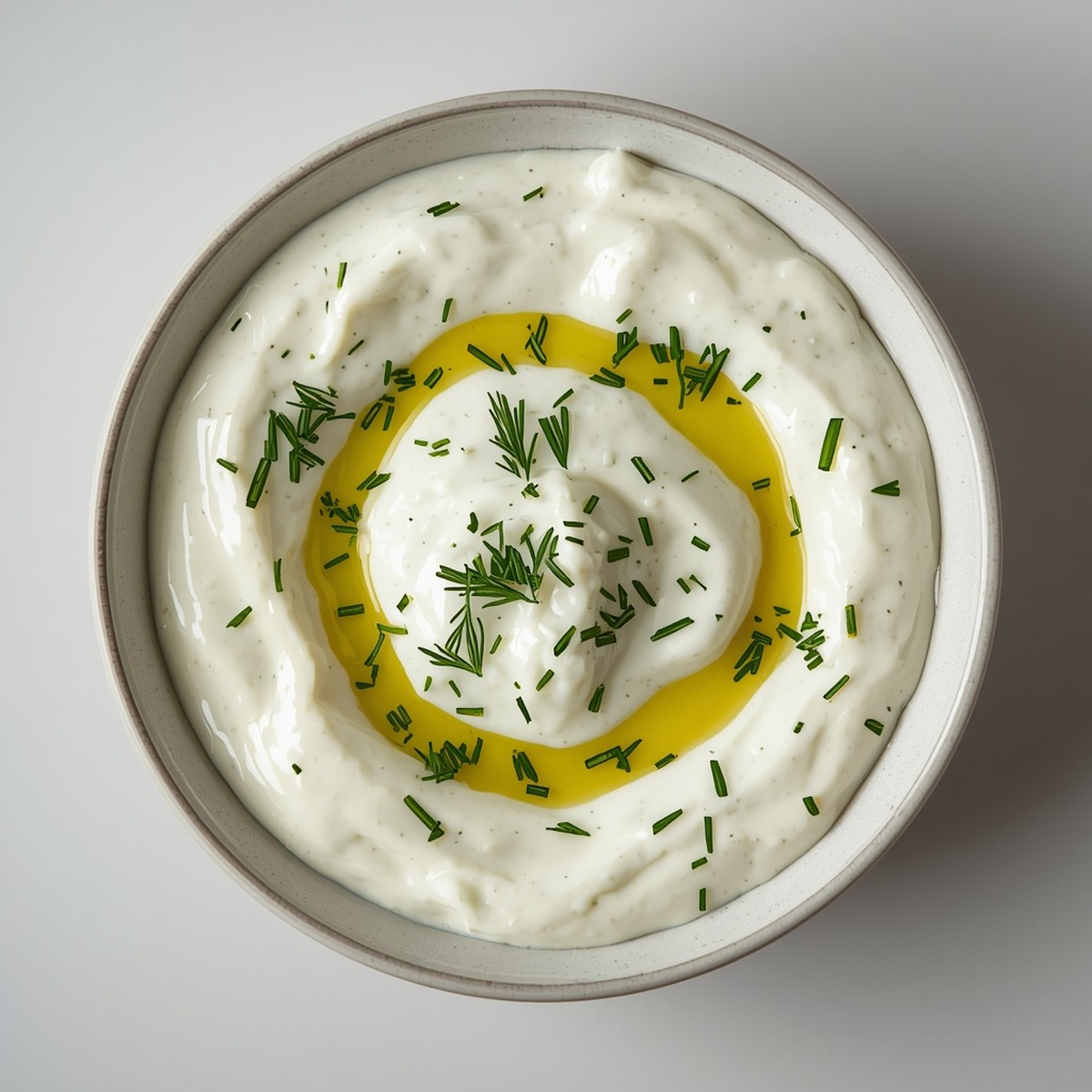 Overhead close-up of tzatziki sauce in a bowl with creamy texture, garnished with fresh dill and olive oil