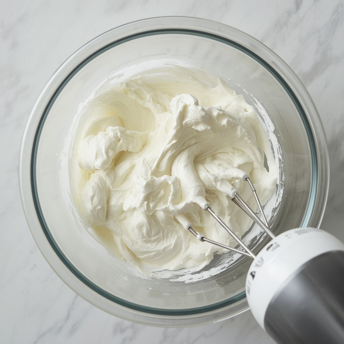 bowl of whipped egg whites with a hand mixer forming stiff peaks