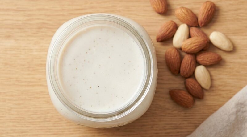 Glass jar of homemade almond milk with raw almonds on a wooden surface